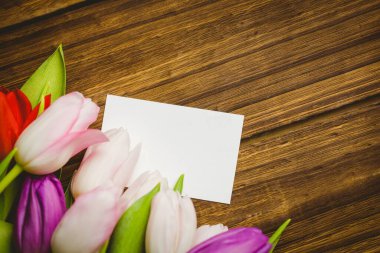 Boş, beyaz, dikdörtgen bir kart, tahta bir masanın üzerinde, renkli bir lale buketi ile yatar. Kırtasiye, çiçek, köy, minimalizm, doğa, tasarım, tebrik kartı