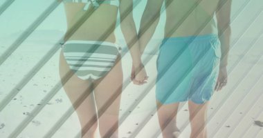 Sahildeki kumlu sahil şeridinde, çizgili bikinili ve yüzme şortlu yürüyen bir çift ayak izi bırakıyor. Romantizm, eğlence, tatil, açık hava, huzur, yaşam tarzı, minimalizm