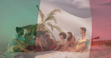 Palmiye yapraklı şemsiyenin altında, kumların üzerinde oturmuş sohbet eden arkadaşlar. Akustik gitarla, plaj havlularıyla. Tatil, tatil, rahatlama, sahil, doğa, arkadaşlık, yaşam tarzı.