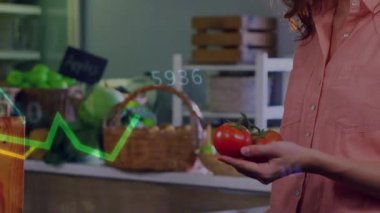 Market satıcısı domates asması kesiyor ve akıllı telefondaki uygulamayı etkinleştiriyor, grafikleri canlandırıyor. Taze ürün, teknoloji, dijital analiz, perakende, çiftlikten masaya, modern, organik