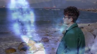 Kıyıdaki adam, mavi ışığın hologram veri kolonu kıvılcımını izleyerek dönen bir teknoloji silindirine dönüşüyor. Gelecekçi, yenilikçi, teknoloji, dijital, görselleştirme, denizcilik, atmosfer