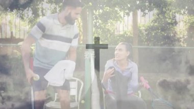 Güneşli kortta tenis molası sırasında bir çift maça ara veriyor ve havluyla su değiş tokuşu yapıyor. Atletik, gevşeme, takım çalışması, açık hava, boş zaman, canlı, sağlıklı