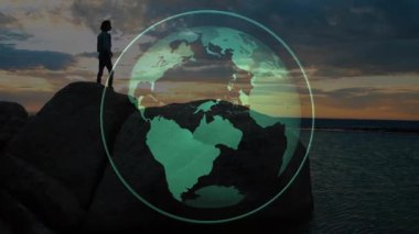 Gün batımı siluetli kadın kayaların üzerinde duruyor. Teknoloji, dünya haritasını gösterirken aynı zamanda arıyor. Macera, keşif, bağlantı, yenilik, açık hava, sükunet, dijital