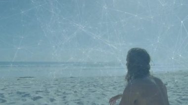 Kumlu sahilde yürüyen ve ağ okyanus üzerindeki teknolojik bağlantıyı resmederken oturan biri. Sahil şeridi, sükunet, dijital bağlantı, rahatlama, doğa, dinginlik