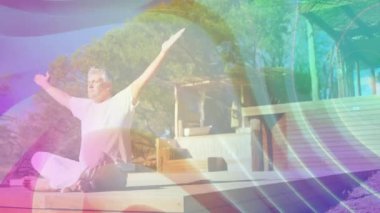 Olgun bir adam, güvertedeki sağlık yoga akışında kollarını kaldırarak nefes alıyor, başınızın üstünde dönen renkler yoğunlaşıyor. Denge, farkındalık, sükunet, açık hava, sağlık, meditasyon, sükunet.