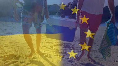 Plaj pikniği için kameraya doğru yürüyen serinletici ve havluları taşıyan iki adamın bayrak kaplaması çekiliyor. Sahil hayatı, arkadaşlık, sahil, boş zaman, açık hava, güneşli, seyahat