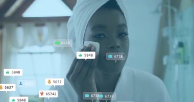 Kadın aynanın önünde yüzünü siliyor ve güzellik dersi sırasında yüzen sosyal medya ölçümleri yaratıyor. Cilt bakımı, bencillik, güzellik, farkındalık, sükunet, dijital, sosyal medya