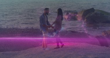 Su kenarında, mor ışık sızıntısı olan kayalık kıyılarda el ele tutuşan çift. Romantik, dinginlik, macera, uyum, sükunet, doğa, siluet