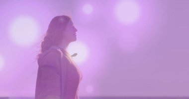 Alacakaranlıkta açık renk ceket giyen ve kıyı şeridinde dokulu süveter giyen pastel gökyüzü ışıltılarıyla bakan bir kadın. Dinginlik, tefekkür, alacakaranlık, minimalist, doğa, sükunet, estetik