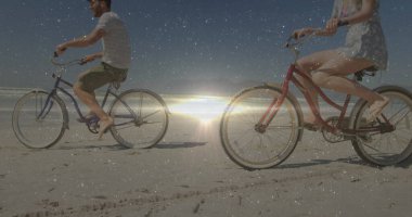 Kırmızı ve mavi kruvazör bisikletleriyle kumlu sahilde pedal çeviren çift. Romantizm, boş zaman, açık hava, manzara, rahatlama, macera, giysi