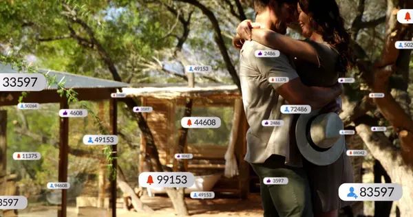 Kabin güvertesi ağaç altında geniş kenarlı güneş şapkası tutan yüzen dijital simgelerle kucaklaşan çift. Romantik, bağlantı, doğa, teknoloji, kırsal, dinginlik, açık hava