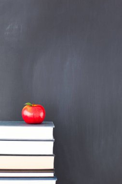 Kitaplarda kara tahtanın önünde kırmızı elma