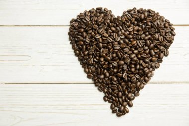 Düz tasarımla boyanmış beyaz tahta üzerinde kalp şeklinde koyu kahve çekirdeği yığını görülüyor. Kahve, kırsal, el işi, fırın, minimalizm, sıcaklık, doku