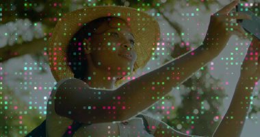 Hasır şapkalı ve tişörtlü bir kadın ormanlık parkta, akıllı telefon ve sırt çantasıyla selfie çekiyor. Doğa, açık hava, günlük, yaşam tarzı, canlı, dinginlik, keşif