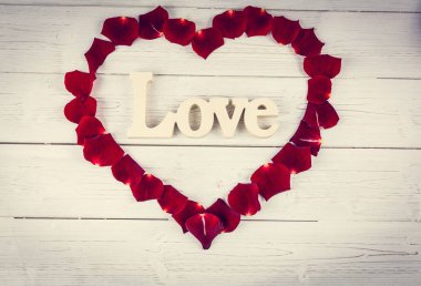 Tahtada kırmızı gül yaprakları olan kalp şeklinde bir çerçeve.