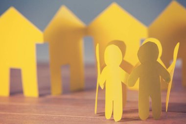 Evleri ahşap masada olan kağıt insanlar.