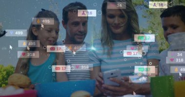 Aile, arka bahçedeki piknik masasında akıllı telefon ve dizüstü bilgisayarla bildirimleri kontrol ediyor. Açık hava, yaşam tarzı, minimalist, teknoloji, eğlence, doğa, bağlantı