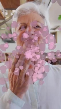 Pembe kalplerin animasyonu, mutlu Kafkasyalı son sınıf öğrencisinin evde video görüşmesi yapması üzerine. emeklilik yaşam tarzı, aşk ve iletişim teknolojisi konsepti dijital olarak oluşturulmuş video.