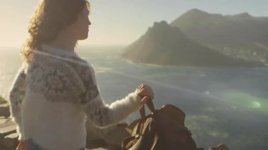 Dişi yürüyüşçünün kayalıklara gelişini gösteren seyahat. Kayışlı sırt çantası deniz manzaralı yürüyüşe hazırlanıyor. Macera, keşif, deniz kenarı, dinginlik, açık hava, manzara, vahşi doğa.