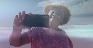 Kıdemli bir kadın kıyı şeridine geliyor. Telefon açısını ayarlıyor. Mercekle selfie çekiyor. Gezgin şehvet, rahatlama, boş zaman, açık hava, canlı, samimi, kıyı