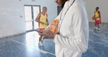 Koç, oyuncular top sürerken ve atış yaparken akıllı telefonları dinleyip basket talimi yapıyor. Sporcu, antrenman, antrenman, modern, spor, egzersiz, takım çalışması