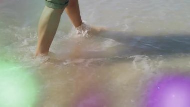 Seyahat reklamı için suya giren insanın bacakları, sürüklenen ışık patlamaları altında dalgalanmalar ve sıçramalar yaratır. Deniz burnu, yalınayak, sükunet, güneş ışığı, doğa, rahatlama, minimalist