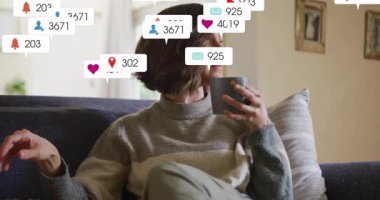 Kadın evinde kanepede kupa yudumluyor pazarlama ikonları üretiyor sonra da köpekleri sakinleştiriyor. Rahatlama, evcil, rahat, farkındalık, evcil hayvan arkadaşlığı, dijital dikkat dağınıklığı, sükunet