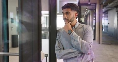 İş koridorunda cam dönüş kapısının yanında duran adam yansımaya ve tarama salonuna tepki veriyor. Profesyonel, modern, düşünceli, kurumsal, gösterişli, iç mimari.