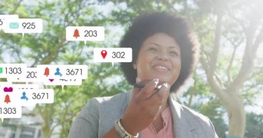 Ağaçların altında konuşan yetişkin bir kadın sosyal medya istatistikleri gösteren ikon kümelerine neden oluyor. Açık hava, iletişim, bağlantı, şehir, canlı, etkileşim, ifade