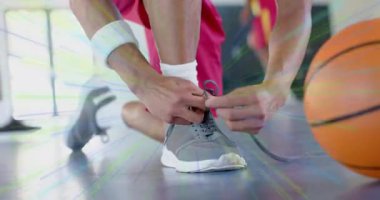 Erkek sporcu, spor antrenmanına hazırlanmak için basketbol sahasında bağcıklarını bağlıyor. Sporcu, antrenman, spor giyim, ayakkabı, odaklanma, hareket, takım çalışması