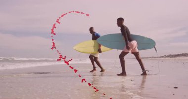Baba ve oğlu sörf tahtaları taşıyarak kıyıda yürüyor sörf reklamları için kalp sarmalı oluşturuyorlar. Aile, bağ, macera, deniz kenarı, arkadaşlık, fitness, deniz