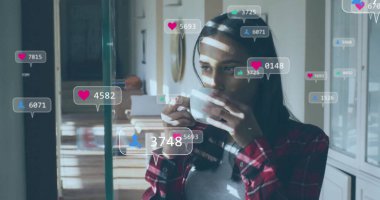 Mutfakta elinde beyaz bardakla kırmızı ekose giyen sosyal medya ikonları olan bir kadın, kopyalama alanı. Günlük, rahatlama, dijital bağlantı, konforlu, modern, yaşam tarzı, refah