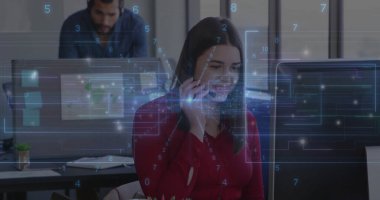 Speaking agent wearing red blouse and headset handling call at office desk, with monitor, papers. Collaboration, communication, modern, professional, workstation, productivity, teamwork