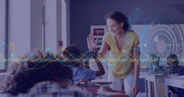 Sarı bluzlu bir öğretmen sınıftaki öğrenci masasına el sallayarak el sallıyor. Eğitim, akıl hocalığı, işbirliği, öğrenme, sınıf, iletişim, ilham