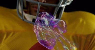 Futbol oyuncusu göğsünde top tutuyor ve spor teknolojisi için miğferin etrafında dönen mor enerji yayıyor. Sporcu, yenilik, fütüristik, eylem, yoğunluk, dijital, dayanıklılık