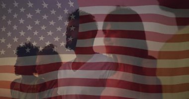 Beş yetişkin alacakaranlıkta kameralar önünde vatansever bayrağını sallayarak birleşme grubunu gösteriyor. Vatanseverlik, birlik, kutlama, alacakaranlık, siluet, umut, manzara