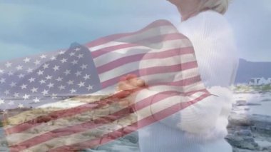 Kıdemli kadın kıyıda duruyor, teknoloji bayrağı solup sallanıyor, çene tarama ufkunu kaldırıyor. Vatanseverlik, esneklik, tefekkür, manzara, dijital örtüşme, dinginlik, olgunluk