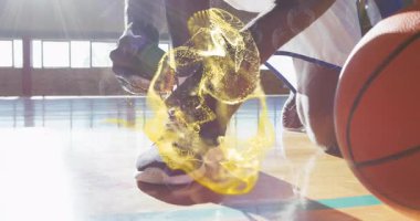 Öndeki oyuncu diz çöküp basketbol ayakkabısı bağlıyor ve altın kıvrımları maça hazırlanıyor. Atletizm, takım çalışması, dayanıklılık, motivasyon, enerji, spor kıyafetleri.