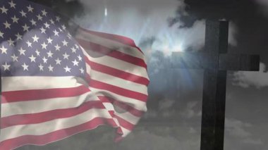 Bayrak kaldırma esintisi, çapraz siluet yakınlarında güneş ışınları altında dalgalanan bayrak şeritlerine neden oluyor. Vatanseverlik, milliyetçilik, ciddiyet, sembolizm, anıt, miras, kumaş