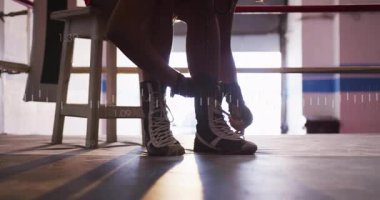 Atlet ayak kaldırıyor ve boks ayakkabılarını ringe bağlayıp antrenman için canlı ölçü güncellemesi yapıyor. Atletik, kararlılık, performans, uygunluk, hareket, minimalist, sağlık