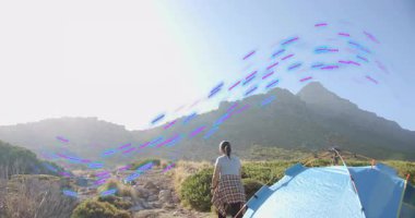 Yetişkin bir kadın yürüyüşçü mavi çadırdan döner ve dağ zirvelerine doğru kayalık tepelerde yürür. Macera, keşif, vahşi doğa, engebeli, sükunet, yürüyüş, açık hava