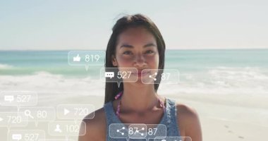 Kadın kıyı şeridi kameraya bakıyor sosyal medya simgelerinin ortaya çıkışını ve güncellemesini izliyor ve gülüyor. Dijital, katılım, minimalizm, açık hava, mutluluk, iletişim, teknoloji