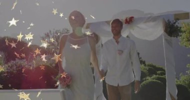 Altın yıldızlı örtüler, gelin ve damat çiçek kemerlerinin altında yürüyor düğün havasını yükseltiyor. Romantizm, kutlama, açık hava, zarafet, neşe, mutluluk, çiçek