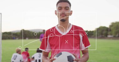 Soccer player holding black-and-white ball on field, with tactical overlay and metal goal post. Athletic, teamwork, strategy, outdoor, vibrant, competition, fitness