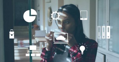 Drinking Asian woman wearing red plaid shirt holding ceramic mug in home office, with tech icons. Workspace, relaxation, modern, professional, digital, interior, calm