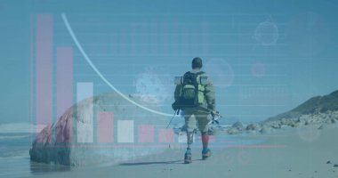 Walking veteran in camouflage on prosthetic legs on beach, with green backpack and fishing rod. Resilience, adventure, outdoor, determination, empowerment, wellness, endurance