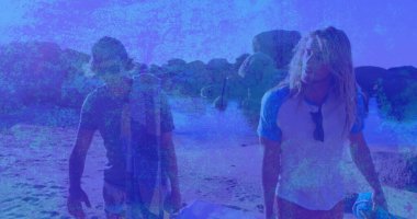 Kayalık kıyı şeridine yakın kumsalda sörf tahtası ve havlu taşıyan iki sörfçü. Güneş parlıyor. Sörf, macera, eğlence, sahil, deniz kenarı, açık hava, eğlence