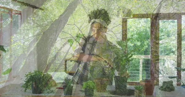 Eğik bitki meraklısı dinlenme çenesi ve güneşli odada saksı bitkileri ve saç bandıyla kameraya bakıyor. Botanik, bahçıvanlık, doğal ışık, iç tasarım, sağlık, sürdürülebilir, yaşam tarzı