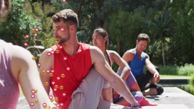 Yoga grubu göletin kenarında gövdelerini büküyor. Üyelerin etrafında yükselen kalp emojileri dokuyor. Sağlık, farkındalık, açık hava, rahatlama, dinginlik, zindelik, doğa.