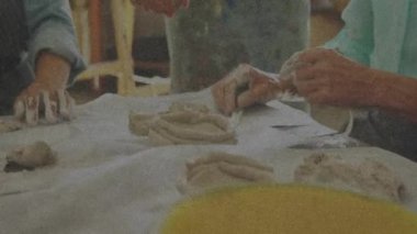 Öğrenciler seramik atölyesinde kil bobinler yuvarlıyor, eğitmen yumru yerleştiriyor ve plaka kullanımını gösteriyor. Sanatçılık, zanaatkârlık, yaratıcılık, eğitim, stüdyo, elle tutulma, ilham